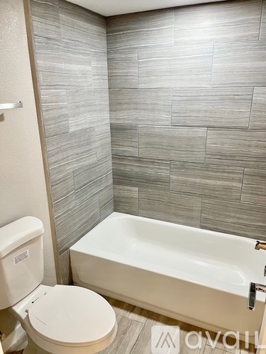 A white toilet sits next to a bathtub in a bathroom with grey tiles.