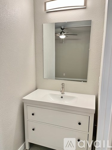 A white bathroom vanity with a mirror and a fan above it.