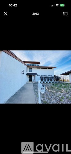A white house with a brown roof and a gravel driveway.