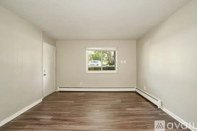 A room with wooden flooring and a window showing trees outside.