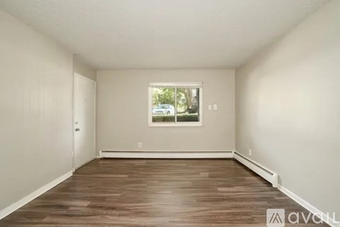 A room with wooden flooring and a window showing trees outside.