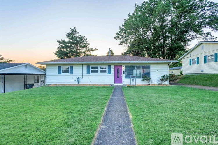 A house with a pink door is surrounded by a grassy lawn.