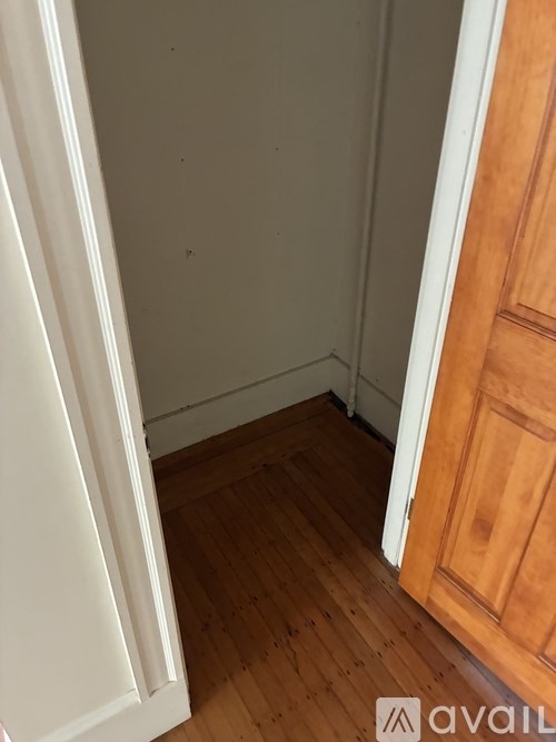 A white door is open to a room with wooden floors and a wooden door.