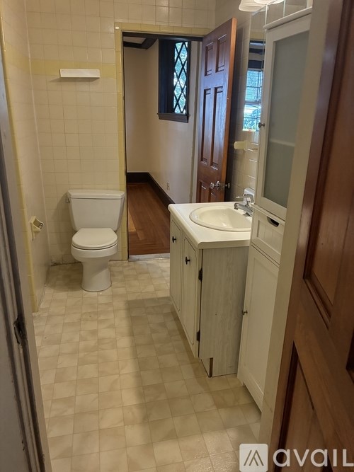 A bathroom with a toilet, sink, and wooden cabinet.