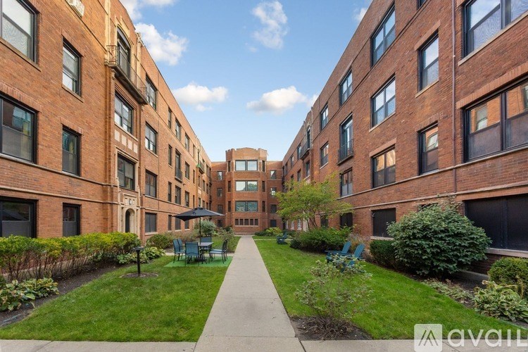 A long walkway separates two rows of red brick buildings with green bushes on the sides.