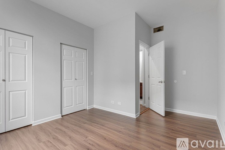 A room with white walls and wooden flooring, with three doors and one open to a hallway.