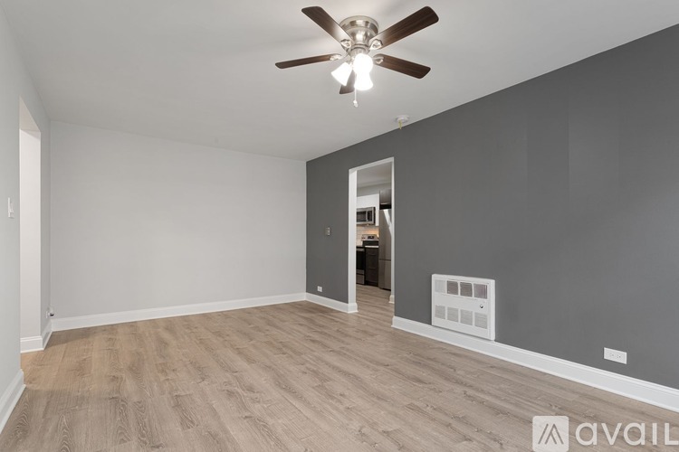 A room with a ceiling fan and light, wooden flooring, and a wall-mounted air conditioning unit.