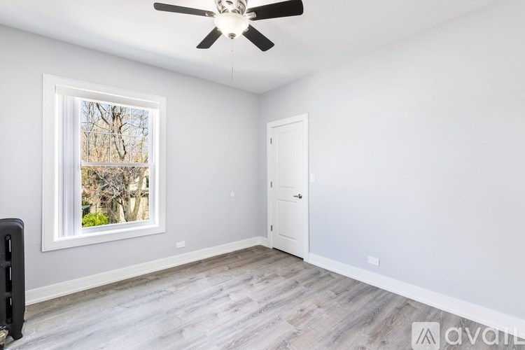 A room with a ceiling fan and a window showing trees and a blue sky.
