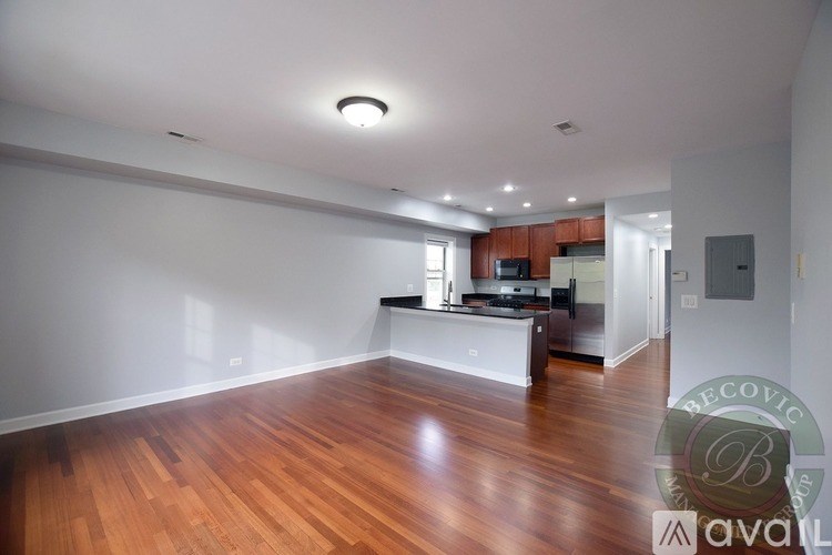 A spacious room with wooden flooring and a kitchen area in the background.