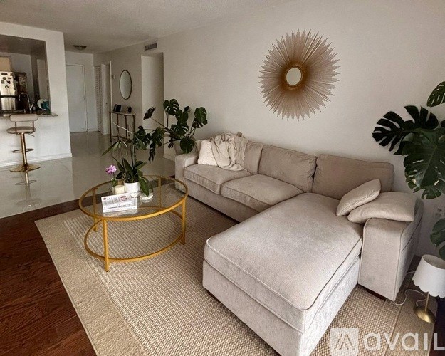 A living room with a beige couch, a gold coffee table, and a large sunburst mirror on the wall.