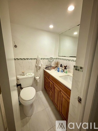 A white toilet is in a bathroom with a white sink and wooden cabinets.