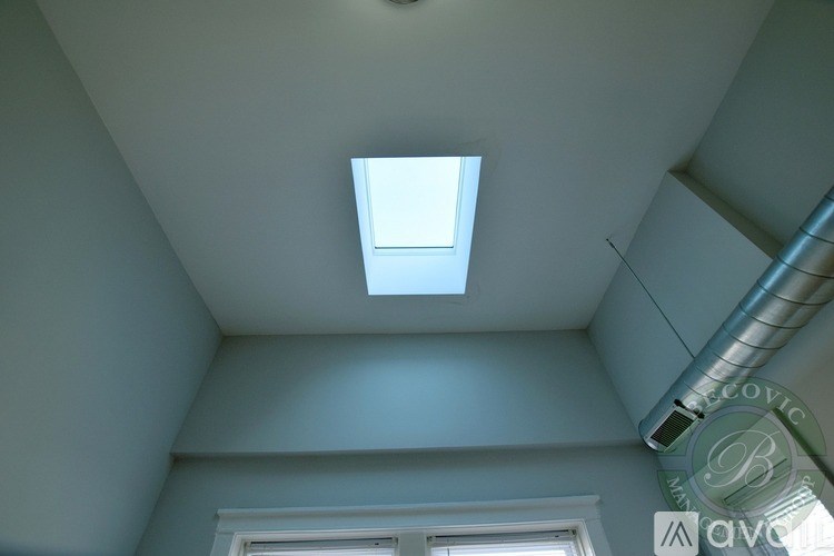 A skylight in a room with a window and a pipe on the ceiling.