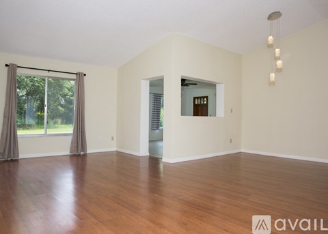 A spacious room with wooden floors and a large window with curtains.