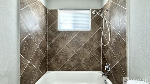 A tiled shower area with a white tub and a window.