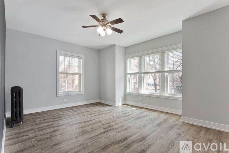A room with a ceiling fan and light, hardwood floors, and two windows.