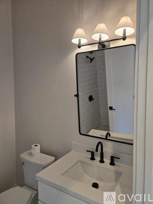 A bathroom with a toilet, sink, mirror and light.