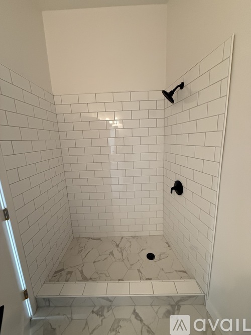 A white tiled shower with a drain in the middle.