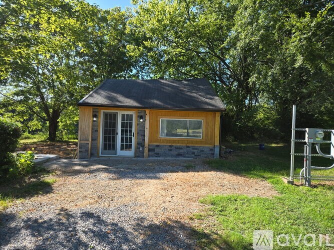 A small wooden house with a black roof and a gravel driveway in front of it.