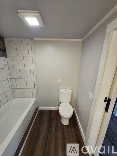 A bathroom with a toilet, tub, and wooden floor.