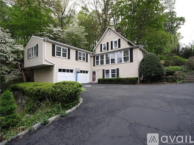 A two-story house with a garage is surrounded by greenery.
