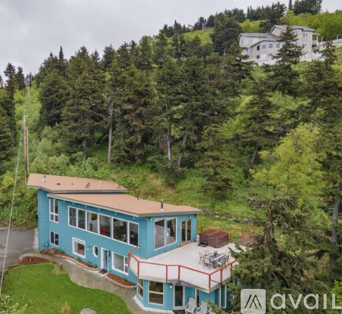 A blue house with a balcony is surrounded by green trees.