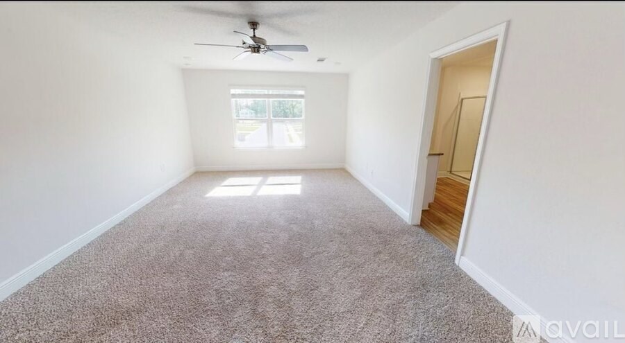 A room with a carpeted floor, a ceiling fan, and a door leading to another room.