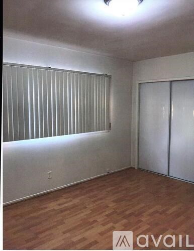 A room with wooden flooring and a white wall with a window covered by blinds.