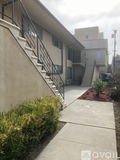 A concrete pathway leads to a house with a metal staircase.