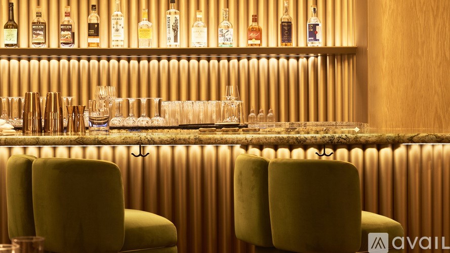 Two green chairs are placed in front of a bar with bottles of alcohol on the shelf.