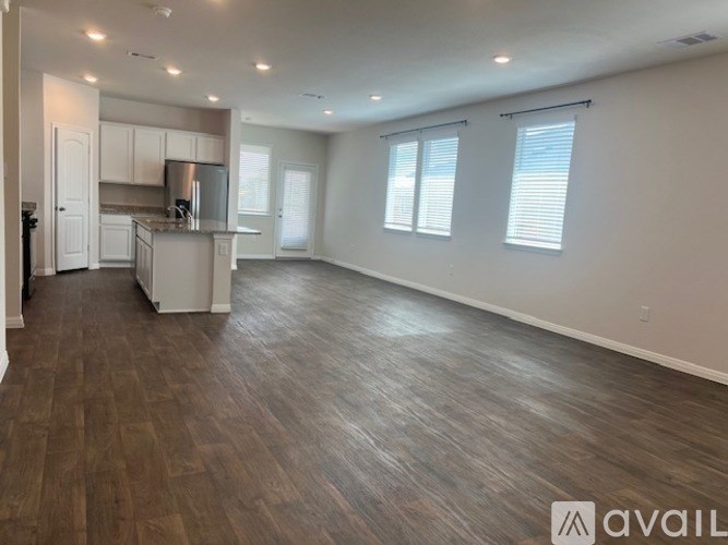 A spacious living room with wooden flooring and a kitchen area in the background.