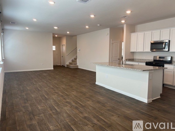 A spacious kitchen and living room with wood flooring and white cabinetry.