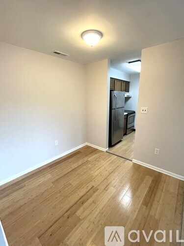 A room with wooden flooring and a kitchen in the background.