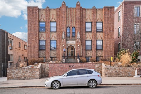 A silver car is parked in front of a red brick building.
