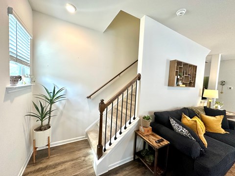 A living room with a couch, a plant, and a staircase.