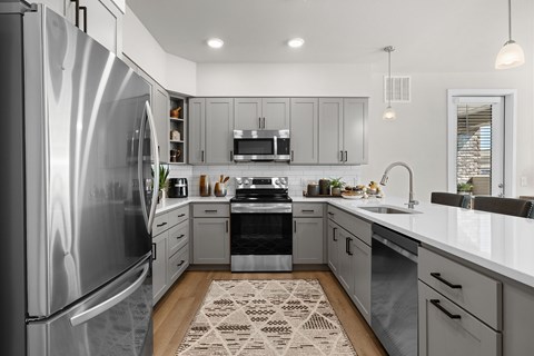 A modern kitchen with a stainless steel refrigerator and a patterned rug on the floor.