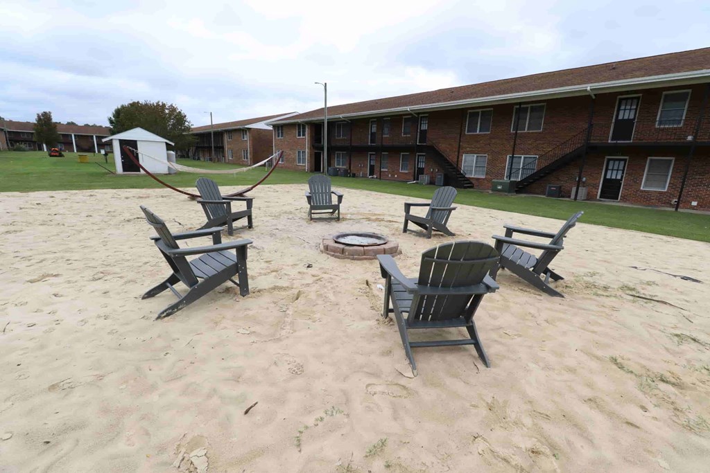 A sandy area with chairs and a table in the middle.