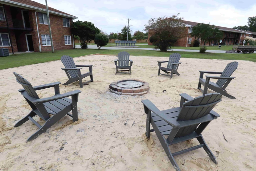 A fire pit surrounded by six chairs in a sandy area.