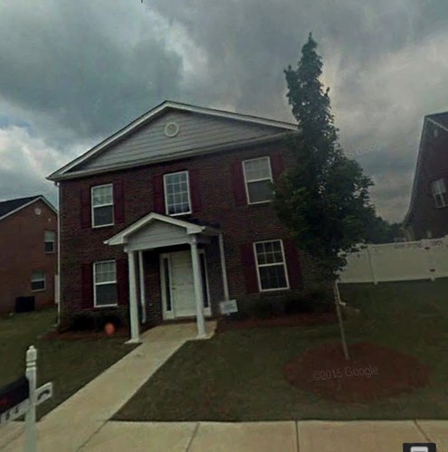 A red brick house with a white door and a tree in front.
