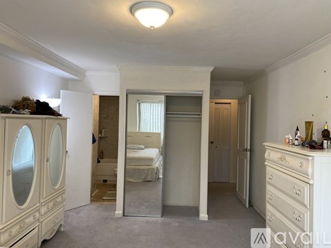 A bedroom with a white dresser, a mirrored wardrobe, and a bed with a white bedspread.