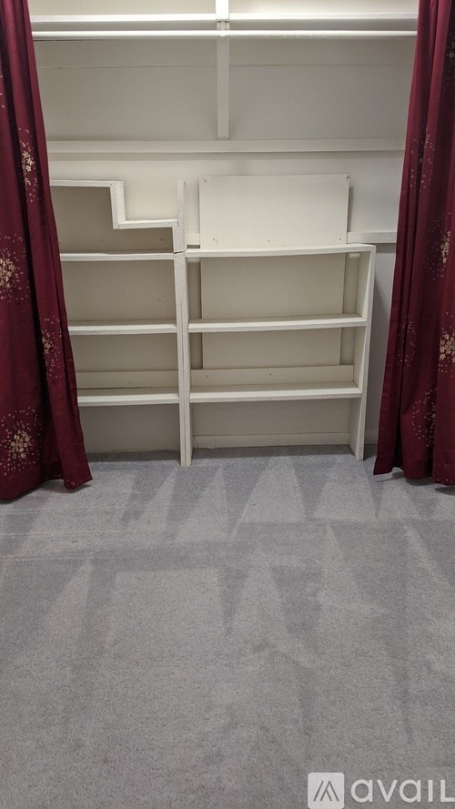 A room with a carpeted floor and a white shelving unit.