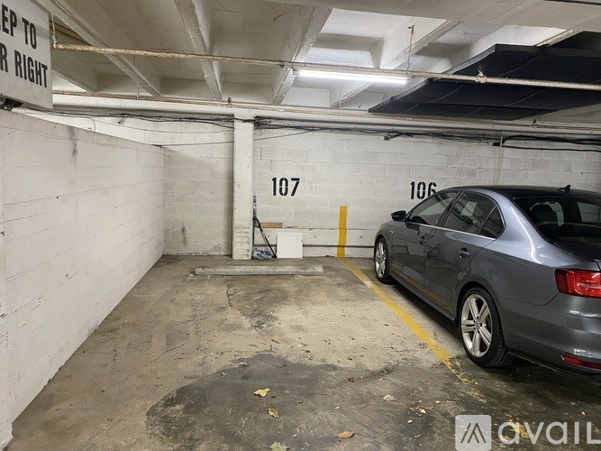 A grey car is parked in a garage next to a white wall with the number 107 on it.