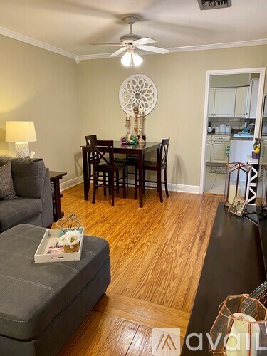 A living room with a grey couch, a wooden dining table with chairs, a ceiling fan, and a lamp.