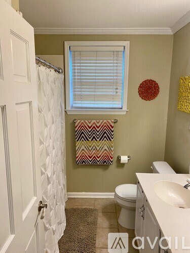 A bathroom with a toilet, sink, and a window with a towel hanging on it.