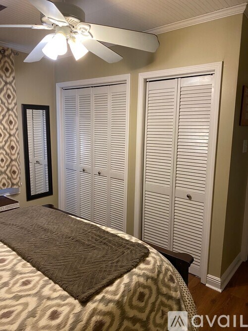 A room with a bed, a fan, and a rug.