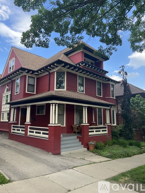A red house with a porch and a tree in front.