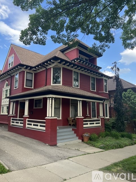 A red house with a porch and a tree in front.