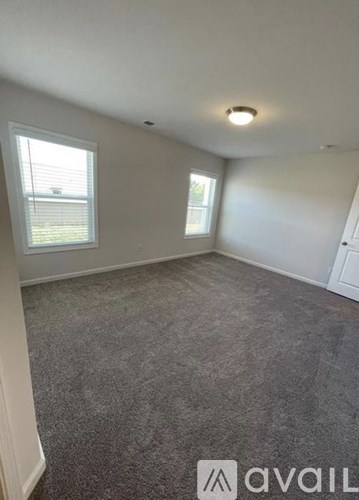 A room with grey carpet and two windows.