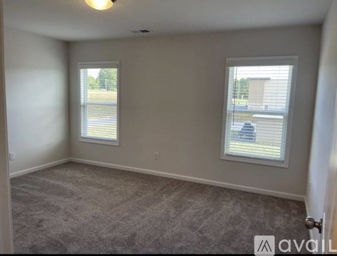 A room with carpeted floor and two windows.