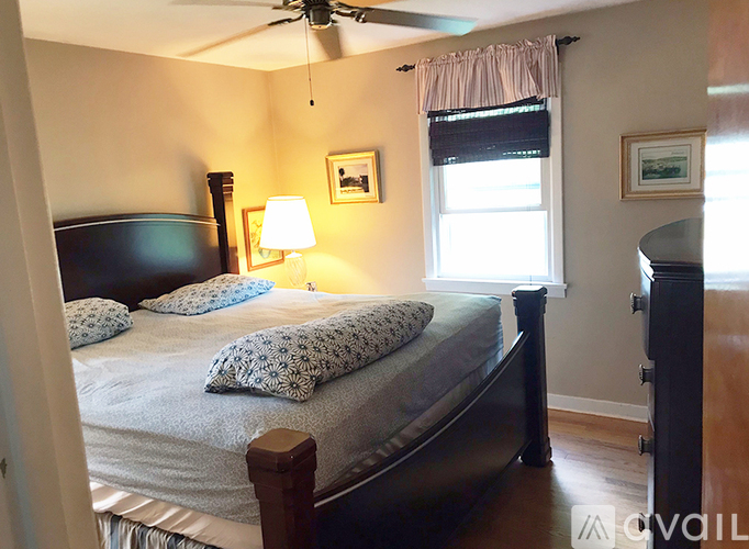 A bedroom with a bed, a ceiling fan, and a window with a curtain.