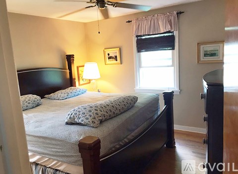 A bedroom with a bed, a ceiling fan, and a window with a curtain.